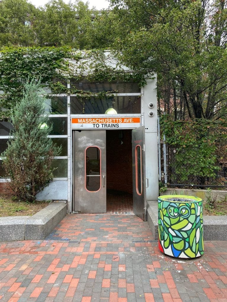 greenery-lined entrance to the Mass Ave MBTA station in Boston with a artistically decorated concrete planter out front