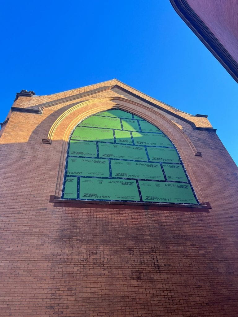 looking up at the side of a church-like brick building with construction paper over a large window