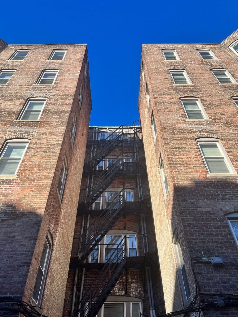 looking up in a brick building alley with metal fire escapes