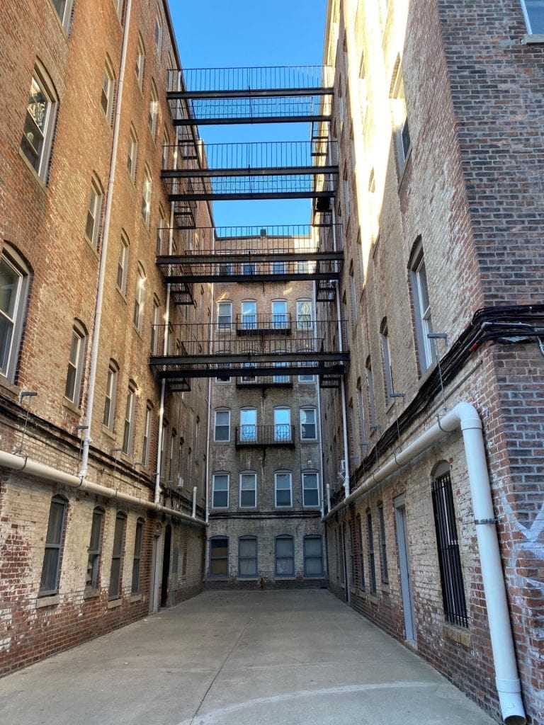 view into a brick building alley with metal catwalk fire escapes