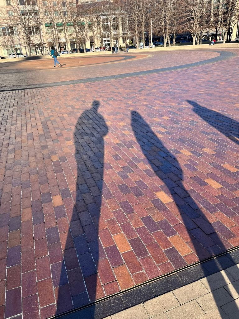 shadows of people cast on a brick plaza