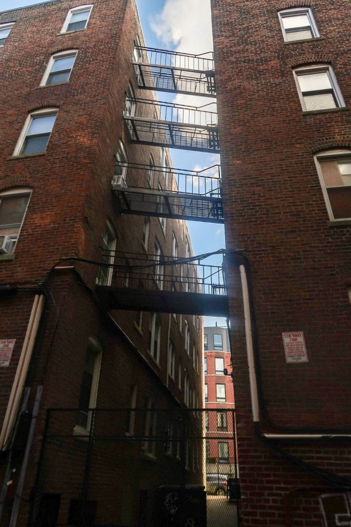 view looking up at fire escapes between brick buildings